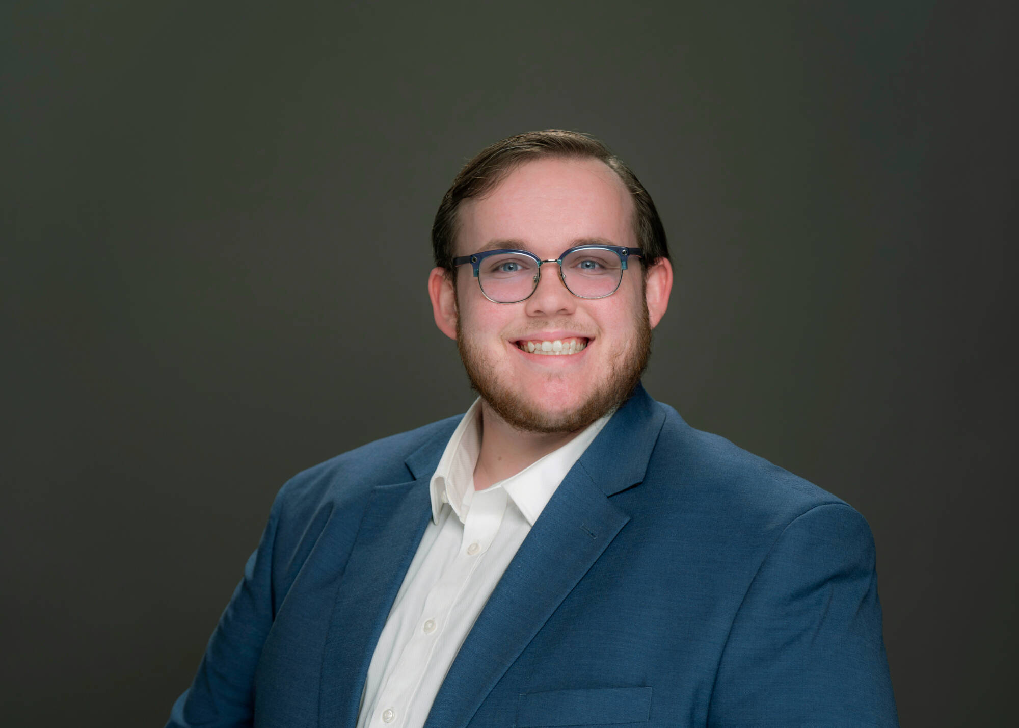 Ben Robar seated for portrait in blue jacket and white, open-collar shirt